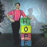 A man in a red shirt stands beside stacked boxes that spell HOPE.