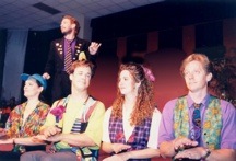 4 adults seated on stage, being directed by a man behind them.